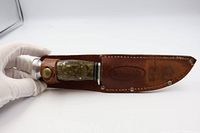 View of the full knife sheathed in brown leather with handle visible showing texture and metal pommel.