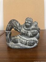 Front angled view of mottled dark grey soapstone carving depicting a seated mother and child fishing