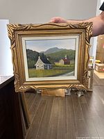 Frontal view of framed oil painting showing house, barn and mountains