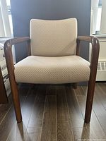 Front view of a fabric covered armchair with wooden arms and legs, light beige upholstery, on a wood floor.