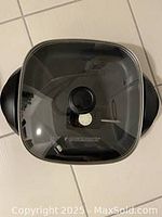 Top view showing the square black cooking surface with glass lid and central knob handle.