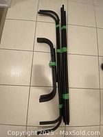 Photo of disassembled black metal clothing rack components arranged on the floor including curved supports and straight rods.