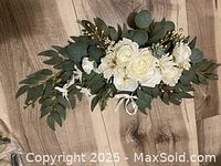Photo shows an off white faux flower arrangement with multiple artificial leaves and small golden decorative accents.