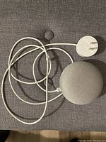Photo of Google Home Mini smart speaker with connected power adapter and cable on a gray couch.