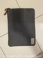 Front view of a laptop carrier case with black and white vertical stripes, zipper closure, leather zipper pull, and a fabric brand label on the bottom corner.