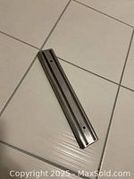Stainless steel magnetic utensil rack lying on tiled floor, showing two mounting holes for screws (two screws missing).