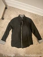 Black zip-up men's shirt laid flat on floor showing front and sleeves.