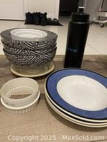 Photo showing large and smaller bowls stacked with plates and water bottle arranged on floor.