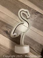 White battery powered neon flamingo light shaped in a standing pose placed on a light wooden floor.