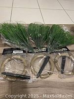 Photo of 6 bundles of green artificial grass sprigs with 6 beige plastic watering stakes, new in original packaging.