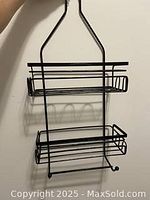 Front view of black metal shower caddy with two shelves and hooks, showing construction and condition.