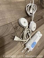 Photo shows two electric toothbrush handles, two round charging bases, and two power cords arranged on wooden surface.