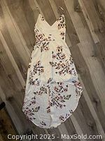 Photo of a white sleeveless women's dress with pink and maroon floral prints laid flat on wooden floor.