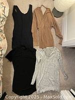 Four dresses and a top laid out on floor; colors: black, beige, gray dresses and white blouse.