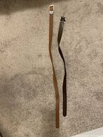 Photo of two women's fashion belts laid out on carpet; one brown with gold buckle, one black with silver buckle.