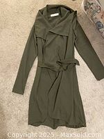 Photo of a women’s jacket laid flat on carpet. Jacket is olive green, size small, with belt and large draped collar.