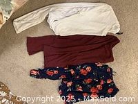 Photo of three women's shirts: white long-sleeve, maroon long-sleeve, and navy blue floral button-up with red flowers