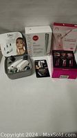 Full lot showing Silk'n Revit device with accessories, DERMAFLASH box, Panasonic pink box, Oozoo illuminator, and eyebrow razors.
