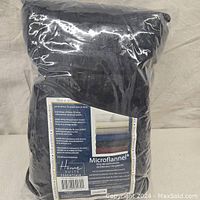 Photo of the original packaging of the bedding set showing black folded microflannel sheets inside clear plastic bag.