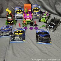Full view of lot showing multiple Batman themed toys including Hot Wheels Batmobiles in packaging, several Batmobile toy cars, and Batman, Robin and Joker action figures with vehicle accessories.