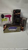 Photo of four boxed hair grooming appliances including pink Conair hair dryer, Curl Secret curling iron, John Frieda Smooth Waves hot curlers, and Esple flat iron.