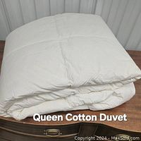 Folded white queen size cotton duvet displayed on a wooden surface, front view showing smooth fabric and stitched pattern.