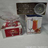 Pressed glass footed tazza on its box, boxed set of four fluted footed hurricane glasses, and boxed glass teacups and saucers set with clear cups and plates.