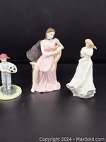 Three Royal Doulton hand-painted bone china figurines displayed on flat surface: a seated woman in pink dress, a boy with a red hat and soccer ball, and a standing woman in white dress.