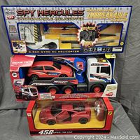 Photo of the full lot showing the Spy Hercules unbreakable helicopter at the top, the Dickie Toys Hotrax flatbed tow truck with a red car in the middle, and the 458 Super The Car model car at the bottom, all in their original packaging.