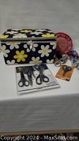Vintage daisy print fabric sewing basket with some sewing accessories and scissors displayed around it on a white surface.