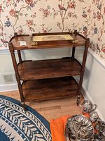 Front view of the wooden serving cart with removable tray placed on top near wallpapered wall.
