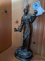 Full view of the bronze figure showing the woman standing with a bird on her left hand and another bird in her right hand, detailed long dress, and feathered headpiece.