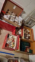 Overview photo showing five cardboard boxes on the floor, each filled with various vintage Christmas tree ornaments packed with shredded paper for protection