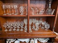 Wide view of all crystal stemware, decanter, and cruet displayed in wooden cabinet shelves.