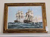 Full frontal view of the framed print showing two sailing ships engaged in battle on the sea with a gilded frame.