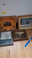 Four framed artworks showing two landscape/seascape paintings in ornate gold frames, one ship painting in simpler frame, and a horse carriage print.