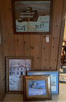 Set of four framed artworks arranged against a wood-paneled wall, showing variety of subjects including barn, house, boats, and a winter landscape.