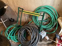 Three garden hoses coiled on the floor, green garden kneeler, and stone fountain base on concrete floor.
