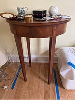 Full view of oval wooden stand with several small items on top, showing four tapered legs and oval top surface.