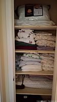 Overall view of five shelves in the linen closet showing folded bedding items including pillows in packaging, sheets, and comforters.