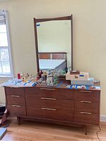 Front view of the dresser with mirror attached and various small items on top.