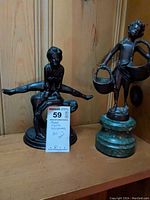 Photo of two metal figure sculptures on a wooden surface showing the acrobats and boy with baskets.