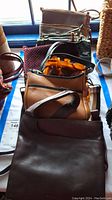 Overview of 6 assorted purses and handbags including leather and cloth materials in various colors and sizes on a table.
