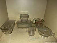 Photo showing the full assortment of three glass refrigerator boxes with lids, two glass measuring cups, and a glass juicer arranged in a cabinet area.