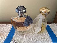 Pair of perfume bottles side by side on a lace cloth; Shalimar Parfum Initial and Des Lys Eau de Toilette.