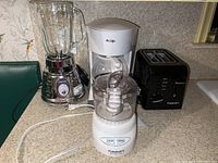Full view of lot on kitchen counter showing Chrome Osterizer blender with glass pitcher, white Mr Coffee drip coffee maker, black Cuisinart toaster, and white Cuisinart Mini-Prep Plus food processor