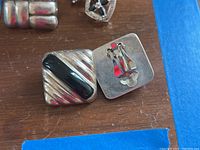 One square silver-tone clip-on earring with black diagonal inlay, shown from front and back with markings visible