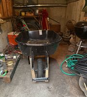 Front view of the black wheelbarrow showing the single front tire, metal frame, and black tub.