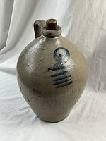 Front view of the salt glaze ovoid jug with visible blue swirl decoration and wooden stopper on top.