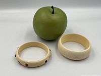 Wide and studded bangles side by side with apple for scale